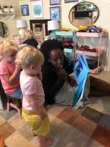 An early childhood educator sits on the floor with children in her program. Together they engage with a book, looking intently at pages and interacting with the material.