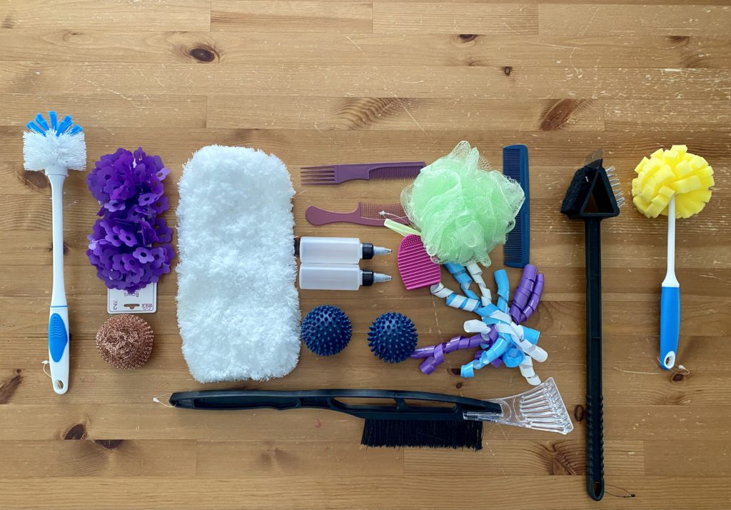 Viewed from above, a table is covered in adaptive art supplies including brushes, scrapers, sponges, fidgets, combs, and more.