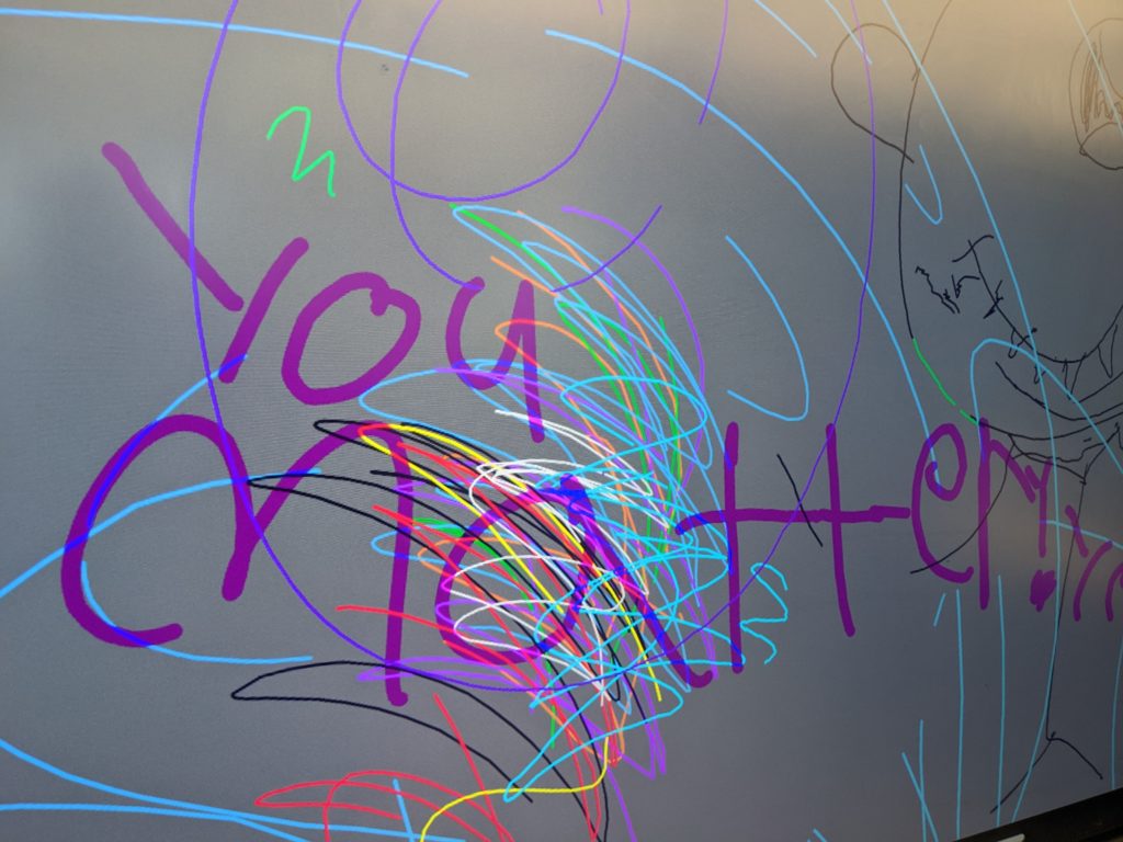A smart board in a classroom with drawings and lines, and in purple, writing that says, "You matter! Yes you do!"
