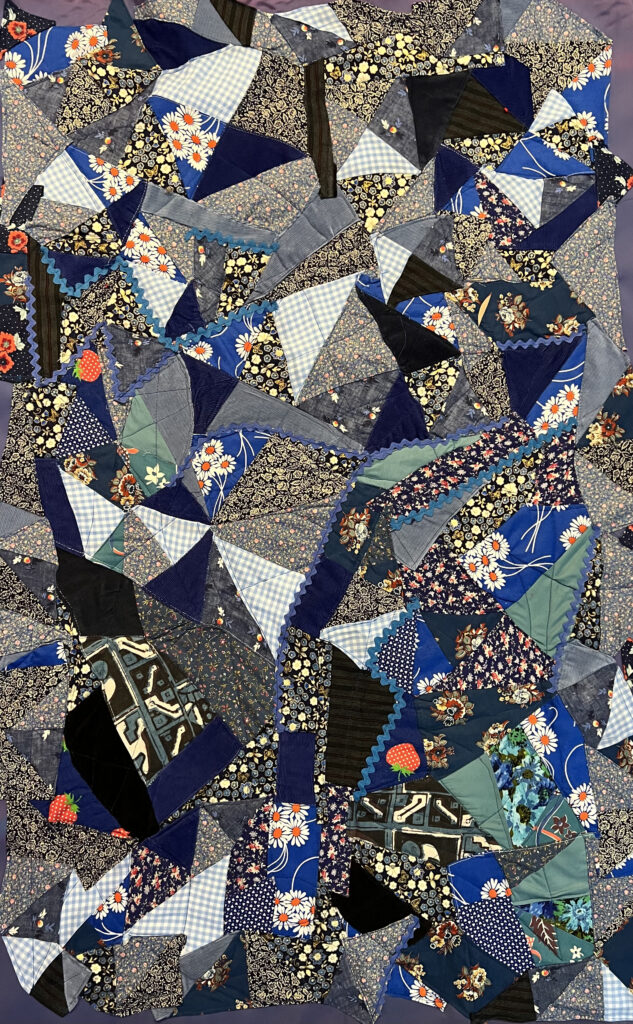 a quilted artwork made from the artists dresses. Many patchwork fabrics in hues of blue and differing designs. 