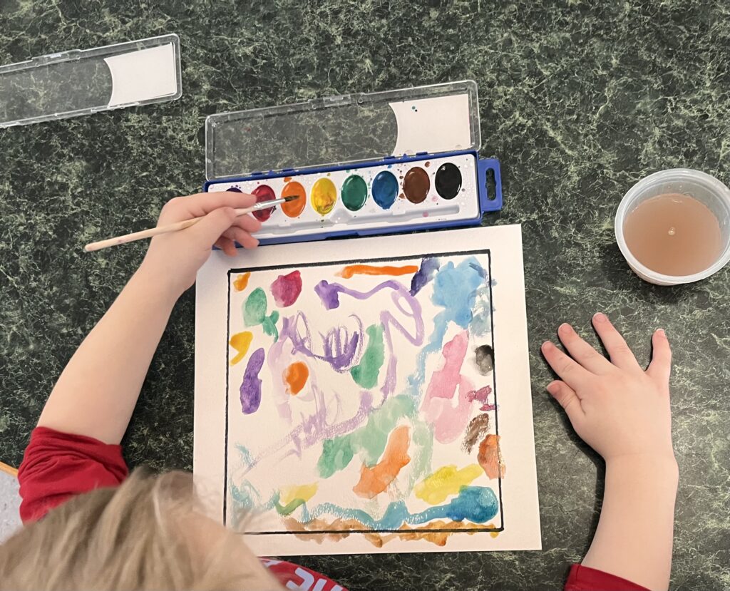 Photo from a recent provider-led session of Start With the Arts.  Shown are a childrens’ hands painting with watercolors and a multicolored painting in process.